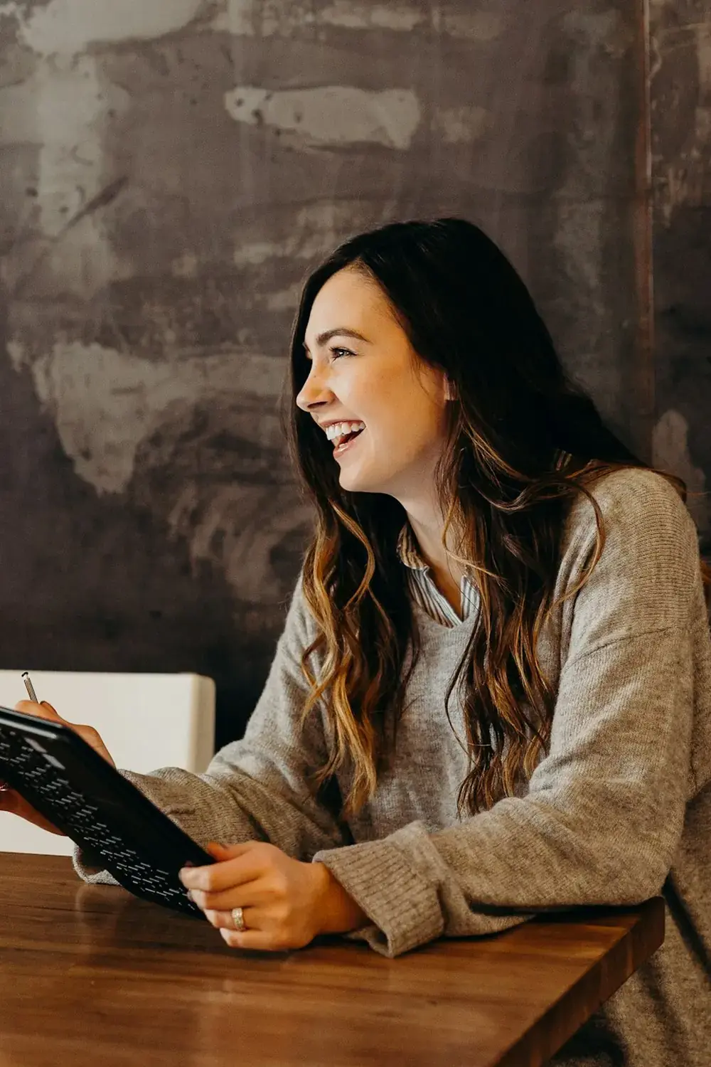 A woman laughing at a wooden table, a tablet in her hands